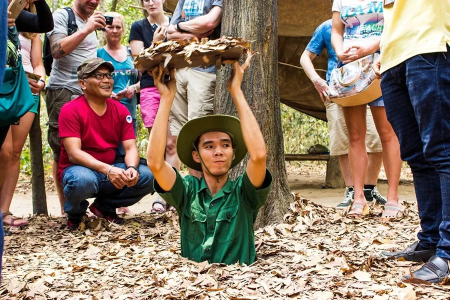 Travelers experiencing a hidden tunnel entrance demonstration during a cultural and historical tour in Cu Chi.