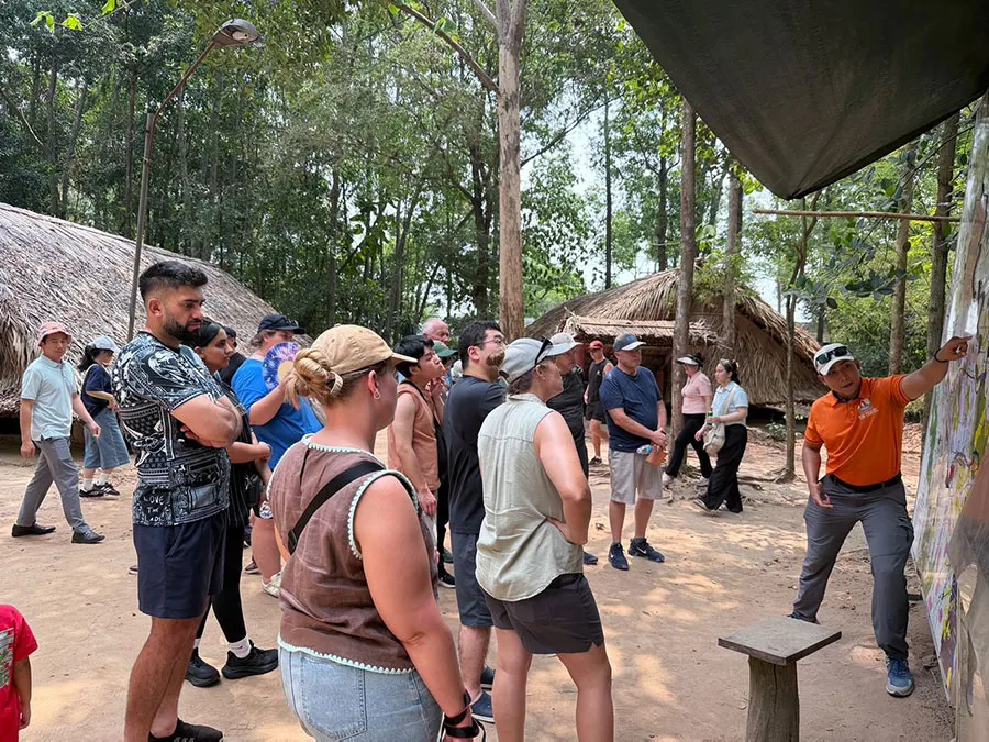 International travelers attentively listening to historical stories during their Cu Chi Tunnels guided tour with Saigon Adventure.