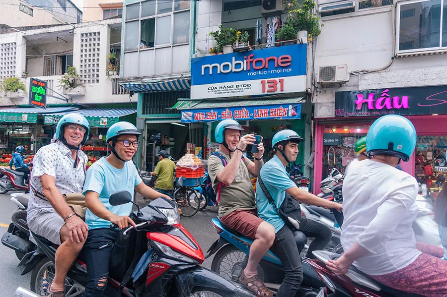 Tourists enjoying a Saigon scooter tour through busy local streets in Ho Chi Minh City