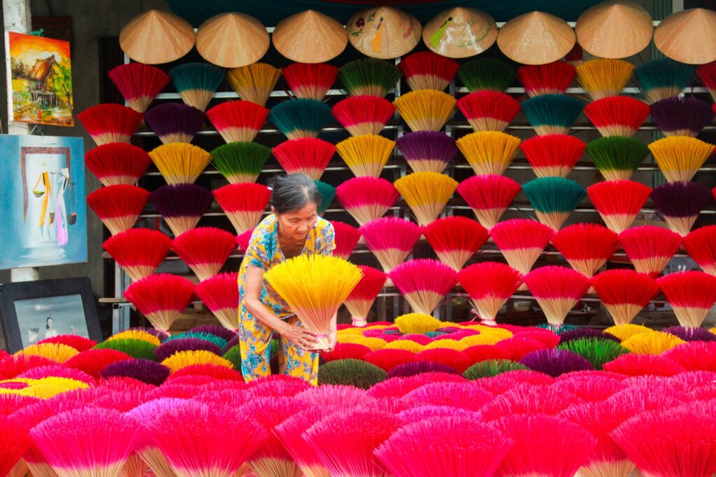 A local woman arranging vibrant, colorful incense sticks and traditional conical hats at a village in Hue, Vietnam.