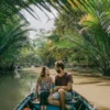 A smiling couple taking a scenic boat tour through a narrow, palm-fringed canal in the Mekong Delta, Vietnam.