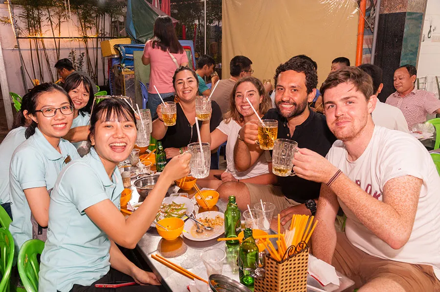 Tourists happily enjoy a meal with their local guide at a bustling night food market.