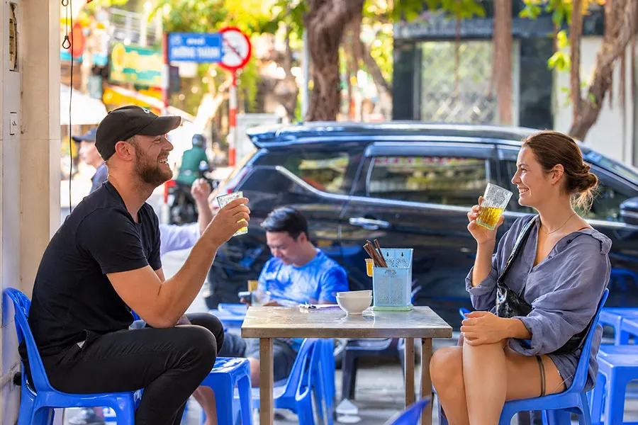 Bia hoi in Hanoi: How to order, what to eat and what it costs 2 Travelers relaxing over glasses of bia hoi in Hanoi, enjoying casual conversations and the welcoming atmosphere of a local beer shop.