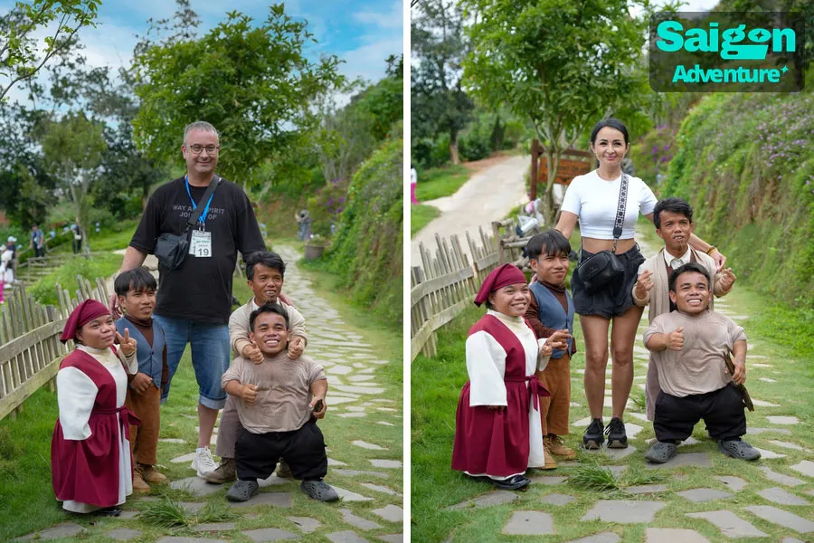 GOD Valley Dalat: Is the Little Village Worth Visiting? 6 Visitors enjoy a fun photo opportunity with performers beside a rustic wooden cottage in GOD Valley Dalat.
